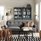 Modern living room: grey ESSEBODA sofa, wooden chair, striped rug, dark bookcase with books.