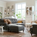 Cozy living room with ESSEBODA gray sofa, white coffee table, wall art, plants, and a bookcase.
