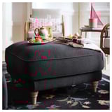 Cozy gray fabric ottoman, wooden legs, tray with tea set atop, spray of pastries, plush chair and rug.