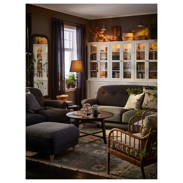 Cozy living room with ESSEBODA footstool, sofa, armchair, rug, coffee table, bookshelf, and plants.