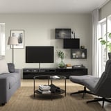 Modern living room with grey sofa, tv, coffee table, books, reeded shelves, large window, curtains, floor lamp.