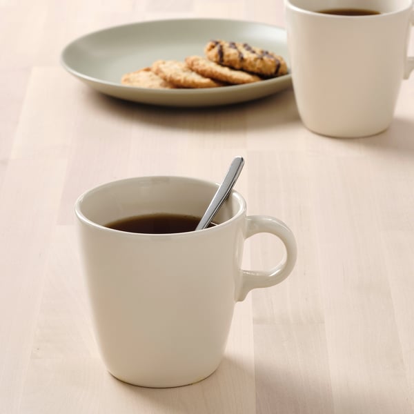 Two white mugs filled with coffee, one with a spoon, and a plate of cookies.