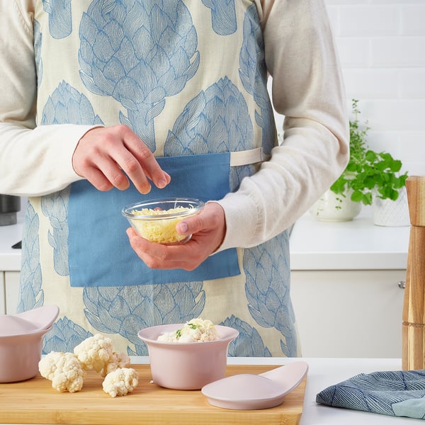 Woman seasoning cauliflower in a FÄRGKLAR dish, showcasing its oven-to-table utility.