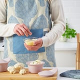 Woman seasoning cauliflower in a FÄRGKLAR dish, showcasing its oven-to-table utility.
