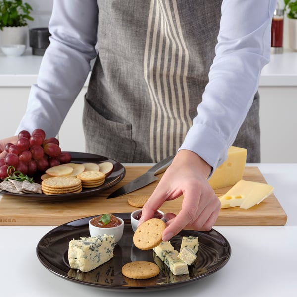 A person assembles a cheese plate using FÄRGKLAR plates, showcasing their versatility and coordination with various foods.