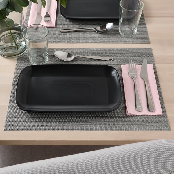 Simple table setting with FÄRGKLAR black plate, cutlery, and glass on gray placemat.