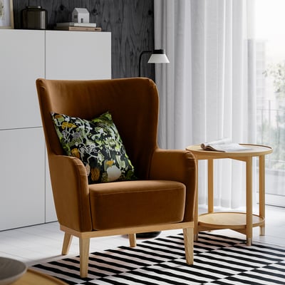 Bright room with FAGERBACKEN chair, brown velvet, high back, next to small wooden side table on striped rug, beside large window.