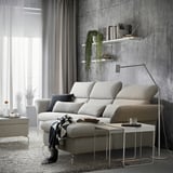 Modern living room with off-white sofa, throw pillows, gray curtains, concrete wall, shelves with books and plant, side table with coffee, and rug.