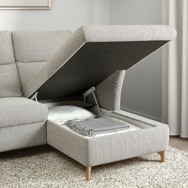 Modern grey sofa with adjustable headrest and open storage compartment, revealing pillows and blanket inside.