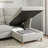 Modern grey sofa with adjustable headrest and open storage compartment, revealing pillows and blanket inside.