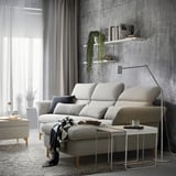 Modern living room with concrete wall, gray curtains, and a light gray FAMMARP sofa with adjustable pillows and white coffee table.