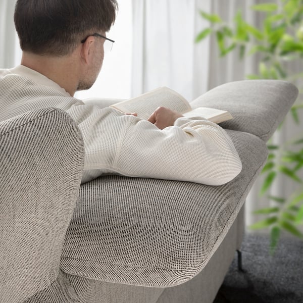 An a person reading, comfortably seated on a FAMMARP beige sofa with adjustable headrests.