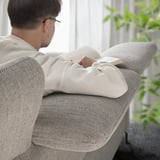 An a person reading, comfortably seated on a FAMMARP beige sofa with adjustable headrests.