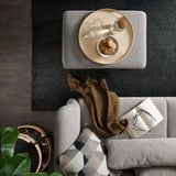 Top view of a modern living room: gray FAMMARP sofa with checkered pillows, wooden coffee table with snacks and glasses, black rug, and potted plant.