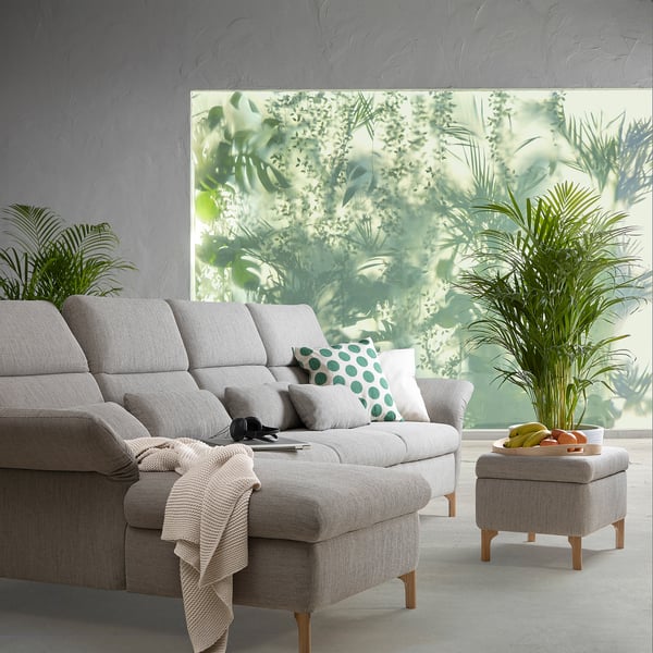 Living room with FAMMARP sofa, green pillows, white throw, and footstool with fruits near window showcasing greenery.
