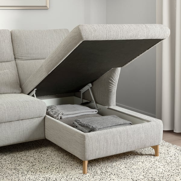 Modern grey sofa with adjustable headrests, open ottoman storage compartment revealing neatly folded blankets.