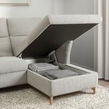 Modern grey sofa with adjustable headrests, open ottoman storage compartment revealing neatly folded blankets.