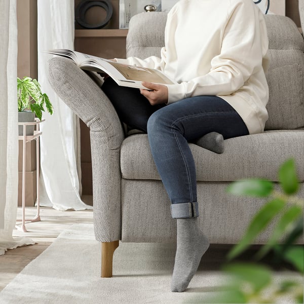 Person reading book on light gray FAMMARP sofa with adjustable armrests and headrests, cozy home setting.