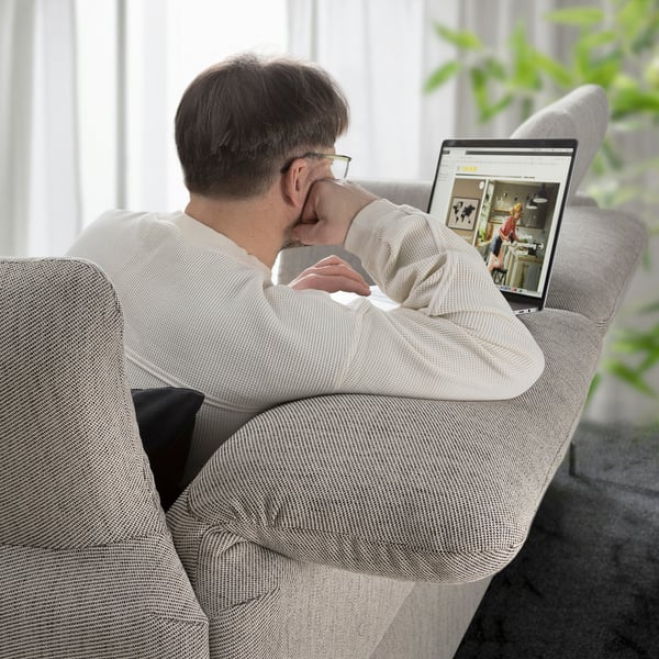 A man on a gray FAMMARP sofa, leaning back with a laptop displaying ikea.