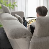 A person sitting on a light grey FAMMARP sofa, working on a laptop with adjustable headrests and armrests.