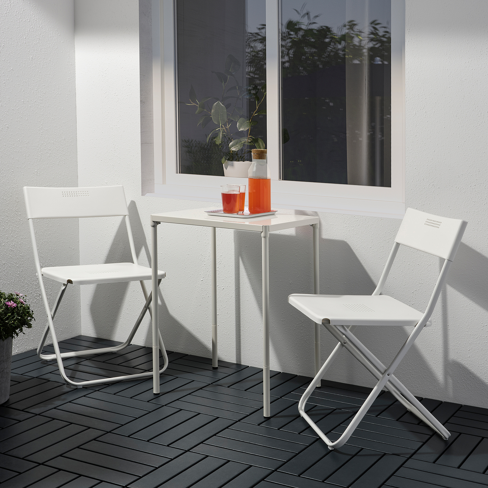 Small outdoor white metal table and chairs set with orange cups, perfect for balconies.