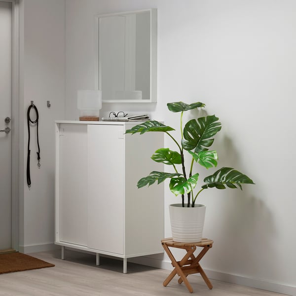 Small FEJKA white potted plant sits on a wooden stool beside a white cabinet with a mirror.