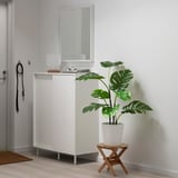 Small FEJKA white potted plant sits on a wooden stool beside a white cabinet with a mirror.