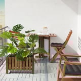 Small balcony with wooden table, two chairs, and FEJKA green artificial plant.
