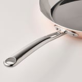 Close-up of high-quality FINMAT frying pan handle, showcasing sleek, polished stainless steel, reflecting durability and elegant design.
