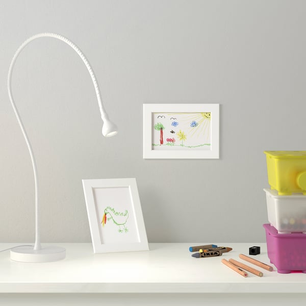 A kids desk with a flexible lamp, drawings in white frames, colored pencils, and containers. The lamp illuminates the workspace.