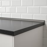 Black water stopper installed against white tiled wall, filling gap between wall and countertop.