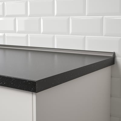 Black water stopper installed against white tiled wall, filling gap between wall and countertop.