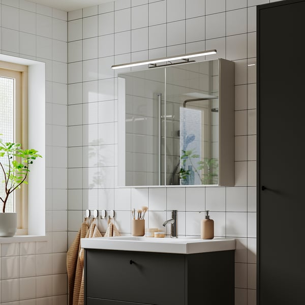 Modern bathroom with lighted mirror, chrome, dark vanity, plants reflecting natural light.