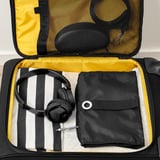 Suitcase open with headphones, a pouch, and a striped cloth tucked inside, showcasing travel organization.