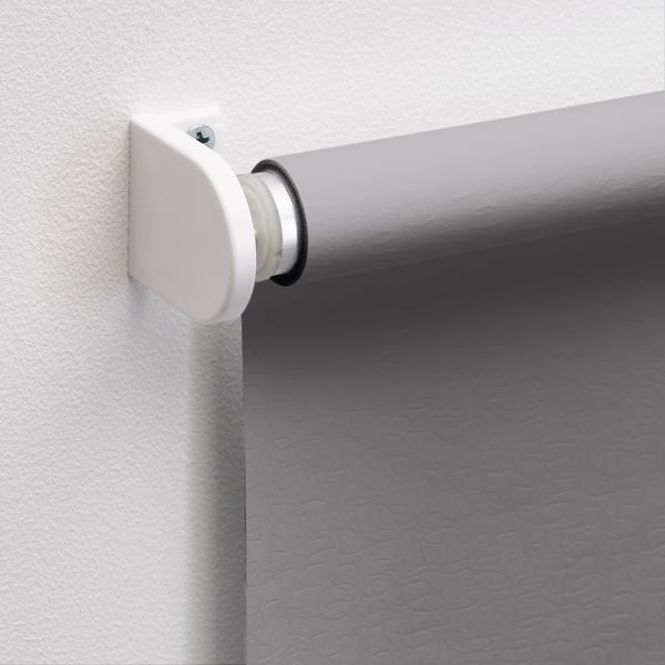 Wall-mounted roller blind bracket, securely holding white rod with circular end cap, attaching blind for light blocking.