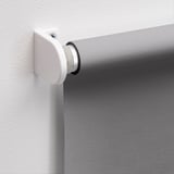 Wall-mounted roller blind bracket, securely holding white rod with circular end cap, attaching blind for light blocking.