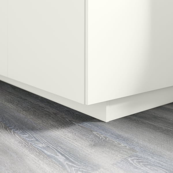 White kitchen cabinet plinth on gray wooden floor. Covers gap between floor and base cabinets. Part of FÖRBÄTTRA series.