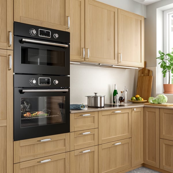 Kitchen with wooden cabinets, black double oven, countertop appliances, and potted plants.