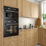 Kitchen with wooden cabinets, black double oven, countertop appliances, and potted plants.
