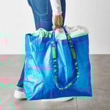 Person holding large blue ikea shopping bag, filled with items.