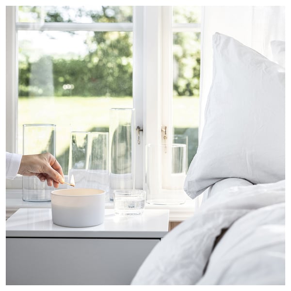 Hand lights white candle near window, with glass vases. Calming, serene indoor setting.