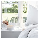 Hand lights white candle near window, with glass vases. Calming, serene indoor setting.