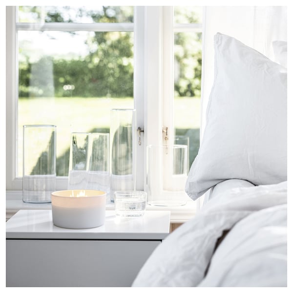A cozy bedroom with a lit candle, bed, and nightstand by a green view.