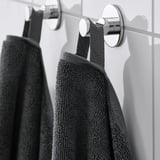 Dark towels hang on wall-mounted hooks. Sleek chrome hooks securely hold thick towels, showcasing their absorbent and decorative design.