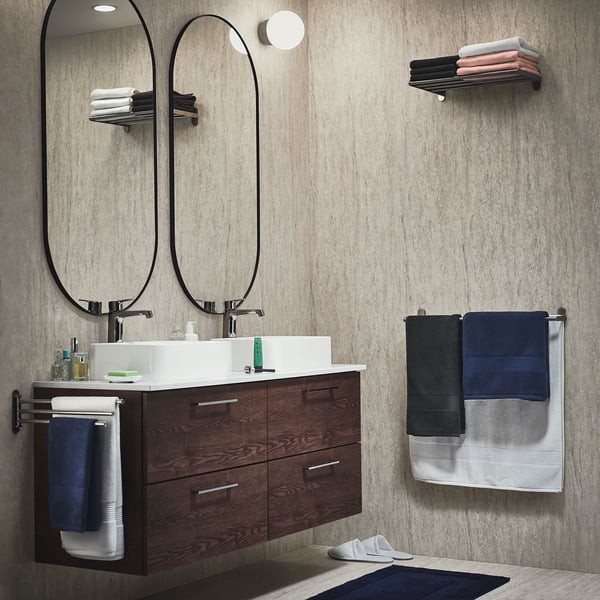 Modern bathroom with FREDRIKSJÖN towels: dark wood vanity, large mirror, dark blue and white towels, concrete wall.