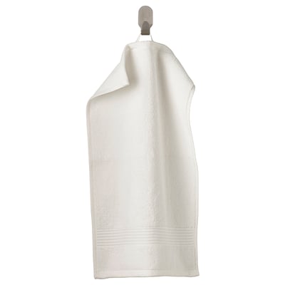 A white FREDRIKSJÖN towel, thick and soft, hangs on a hook. Made of pure cotton, featuring a woven border design.
