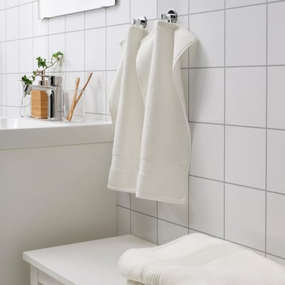 White FREDRIKSJÖN towels hang neatly on wall rack, next to toothbrushes and plant.