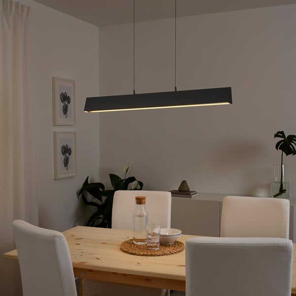 Modern dining area with black FRIDSLUND pendant lamp over wooden table and white chairs.