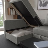 Gray sofa with lift-up storage showing bedding inside. Wall shelves with books above. Dark coffee table in front.
