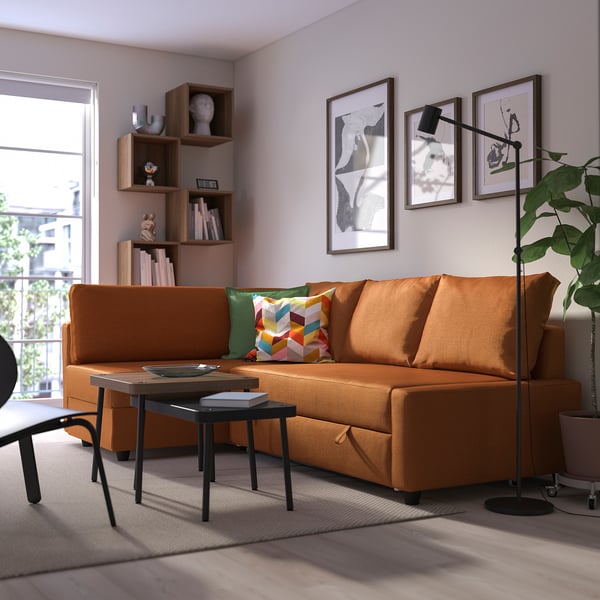 Modern living room with orange FRIHETEN sofa-bed, colorful pillows, coffee table, and wall art. Sofa dominates space.